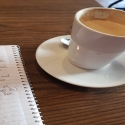 A mug of coffee on a table next to a notebook.